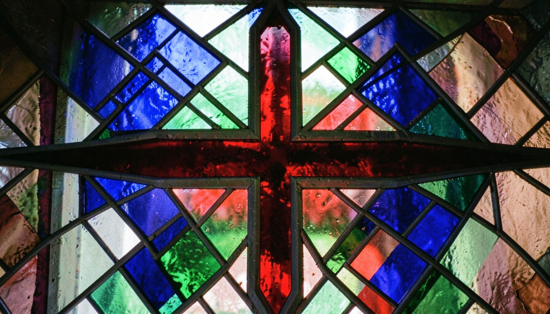 A geometric stained-glass pattern in jewel tones of sapphire, emerald, and ruby with a central cross motif